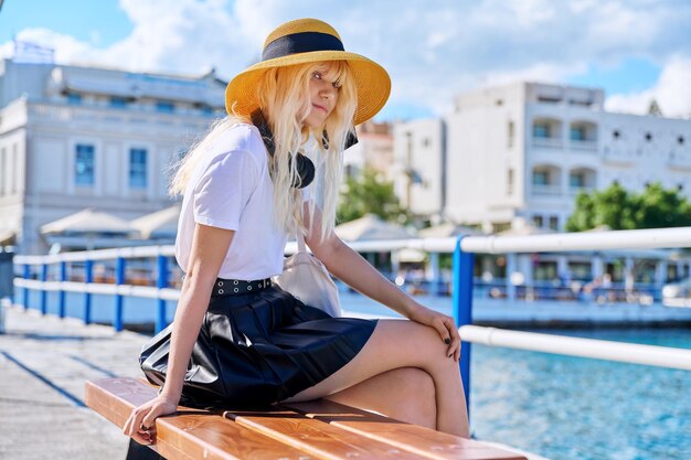 Девочка-подросток в шляпе отдыхает, сидя и ожидая в летнем морском городе
