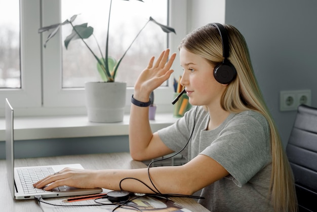 Photo teenage girl in headphones raises her hand while having online lesson at home