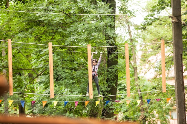 Teenage girl in a helmet and safety equipment in adventure ropes park on the background of nature