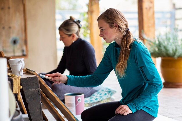 Photo teenage girl and her mother painting wooden shelves blue on a terrace