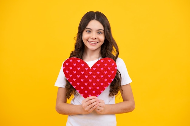 Teenage girl hold shape heart heartshape sign child holding a red heart love holiday valentine symbol isolated on yellow background happy teenager positive and smiling emotions of teen girl