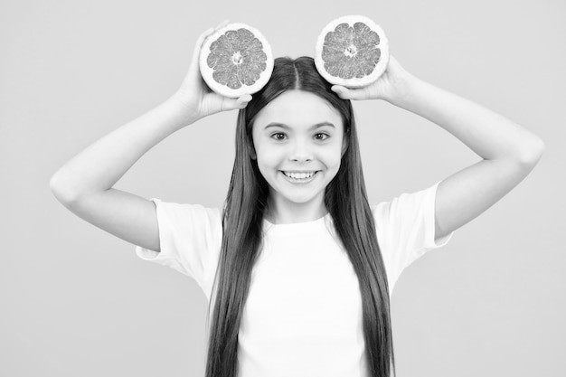 Teenage girl holding a grapefruit on a yellow background Happy teenager portrait Smiling girl