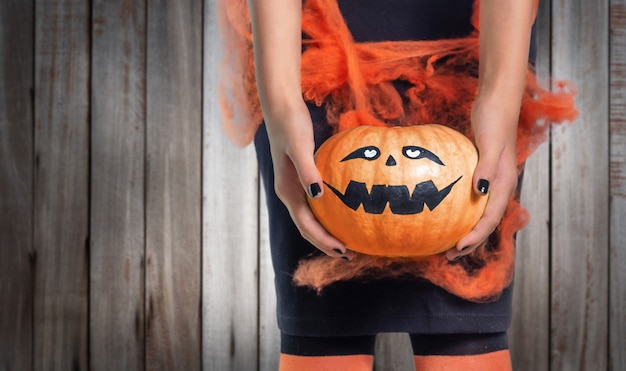 木製の背景に彼女の手でハロウィーンのカボチャを保持している10代の少女