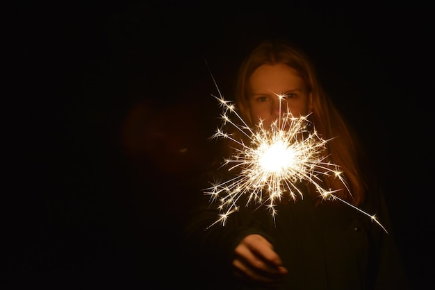 Teenage girl holding sparkler in dark at night