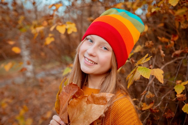 A teenage girl holds a bouquet of autumn leaves in the park in autumn