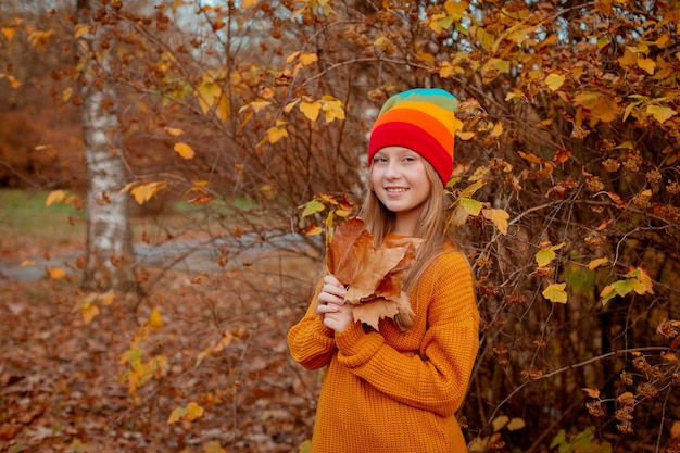 A teenage girl holds a bouquet of autumn leaves in the park in autumn