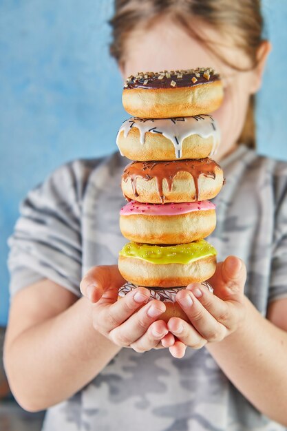 Teenage girl holds stack of multi-colored donuts with two hands.