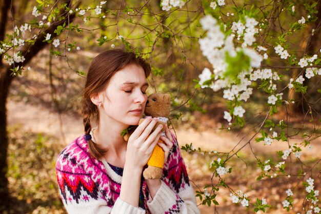 L'adolescente abbraccia l'orso giocattolo nel giardino di primavera. bella ragazza triste faccia con le lentiggini.