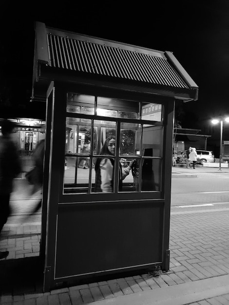 Фото Подростковая девушка в телефонной будке, видная в окно ночью