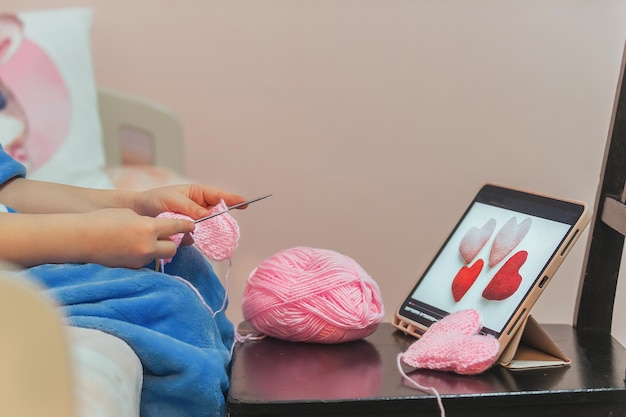 Foto un'adolescente sta imparando a lavorare a maglia, davanti a lei c'è un tablet con un video di formazione