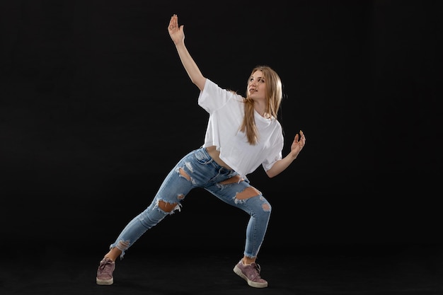 A teenage girl is performing a pose from a dance routine while standing wide apart facing the camera Long blonde hair