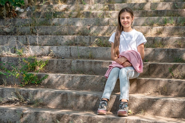 A teenage girl in jeans is sitting on the steps of the stairs on the street