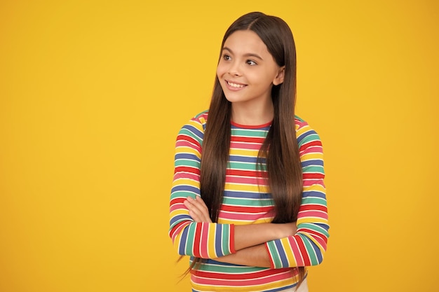 Teenage girl kid with crossed arms looking at camera isolated on yellow studio background Happy face positive and smiling emotions of teenager girl