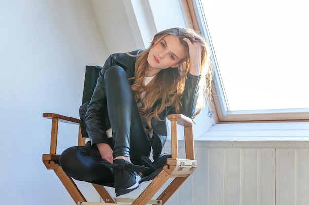 Teenage girl in leather jacket sitting in bright room