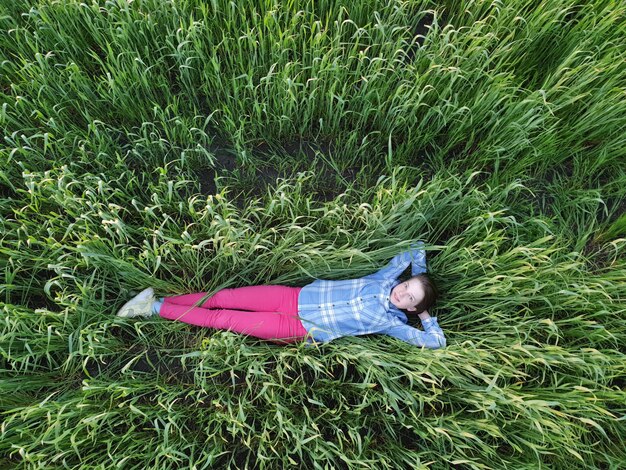 Photo a teenage girl lies in the green grass at sunset, top view, walking and unity with nature