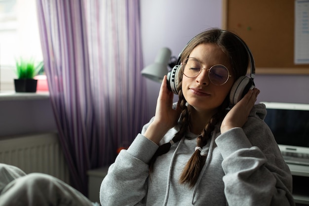 A teenage girl listens to music on wireless headphones with her eyes closed