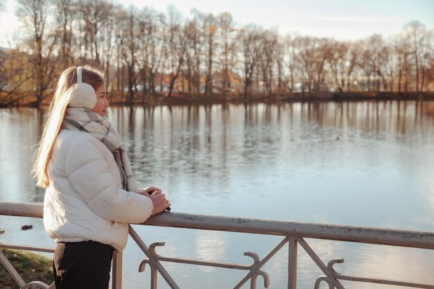 Ragazza adolescente che guarda lontano indossando abiti casual autunnali in un parco autunnale con lago all'aperto