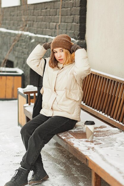 Teenage girl looking away while drinking coffee and sitting on bench in city