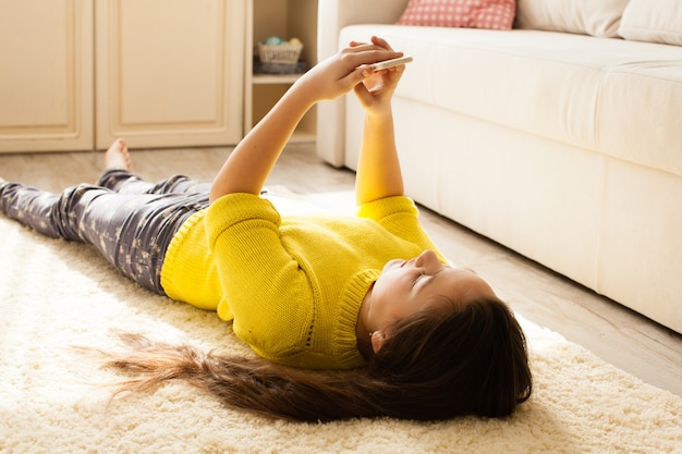 Teenage girl lying on the floor and looks at smartphone