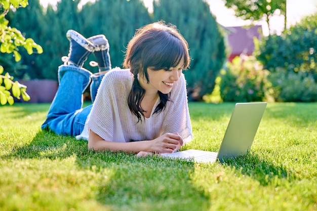 Teenage girl lying on the grass using a laptop