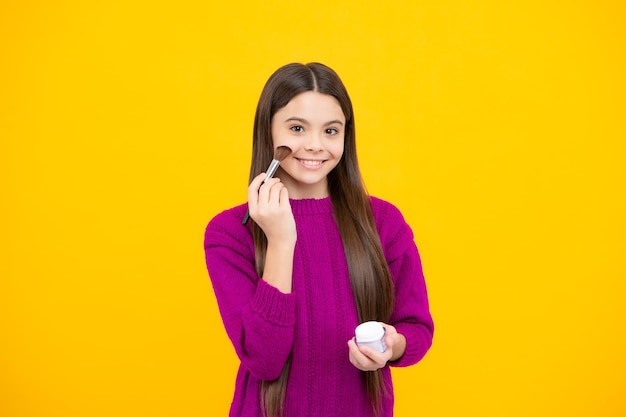 Teenage girl making beauty make up hold powder and brush beautiful teen applying makeup using powder brush isolated on yellow background