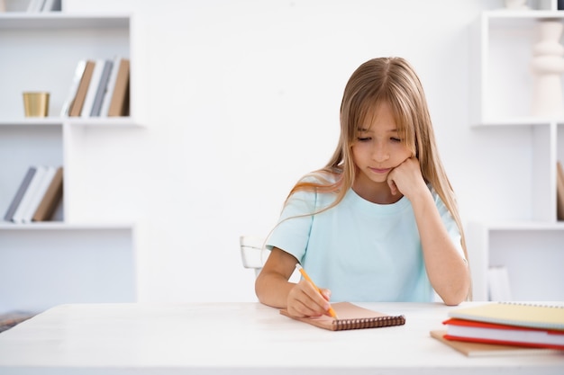 Фото Девочка-подросток делает заметки в блокноте, делает домашнее задание за столом у себя дома