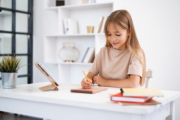 Photo teenage girl making notes in notepad doing homework at table at home