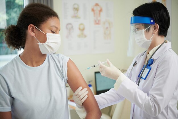 Teenage girl in medical mask vising clinic to get vaccine against coronavirus