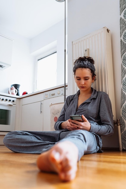 teenage girl in pajamas, with bandage on hair, in home interior, sits on parquet floor in kitchen