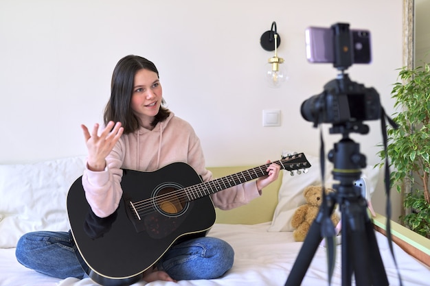 Teenage girl playing an acoustic guitar, talking with followers, recording video for channel, blog. Hobbies for girls, music, art, education, online communication with children and adolescents