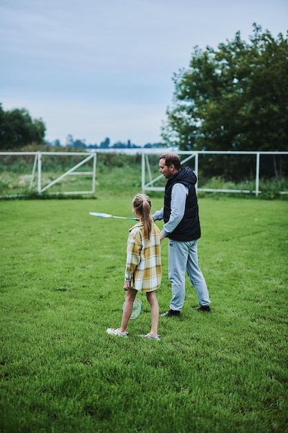 teenage girl playing badminton with her father on green grass in summer park