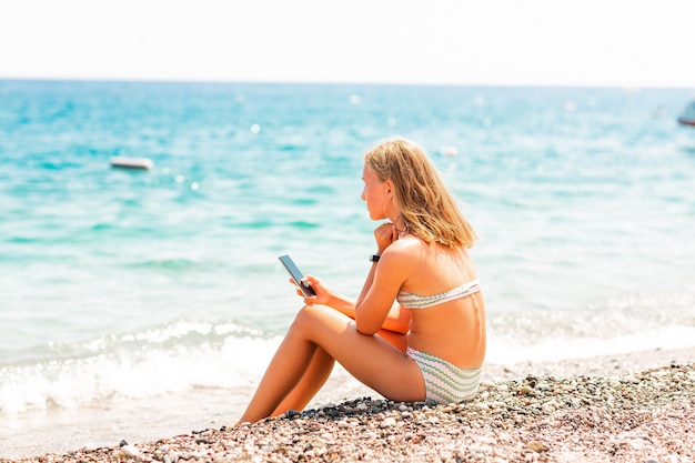 Adolescente che gioca e che cerca web al telefono sulla spiaggia