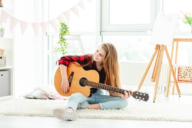 明るい部屋の床に座ってギターを弾く10代の少女