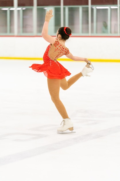 Teenage girl practicing figure skating on an indoor ice skating\
rink.