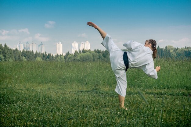 Teenage girl practicing karate kata outdoors, performs the uro mawashi geri (hook kick)