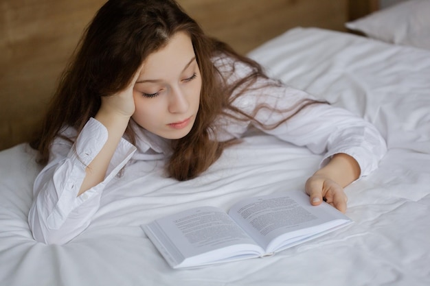 Teenage girl reading a book lying on the bed