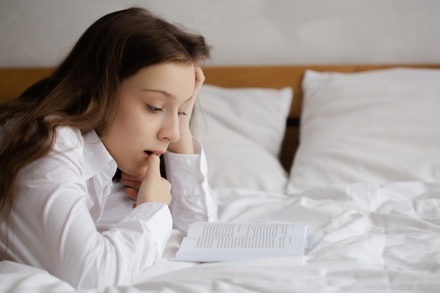 Teenage girl reading a book lying on the bed