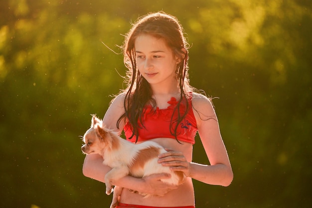 A teenage girl in a red swimsuit with a dog in her arms A girl and a chihuahua near the river