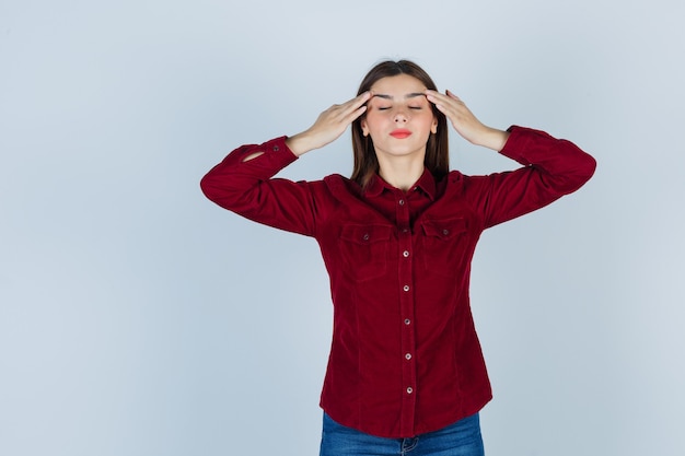 Teenage girl rubbing temples in burgundy shirt and looking relaxed. front view.