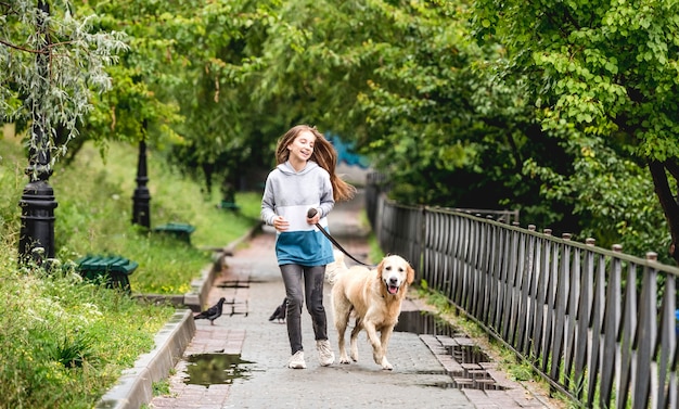 Teenage girl running with golden retriever dog in park after rain