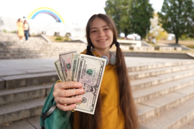 A teenage girl shows a lot of dollar bills and smiles