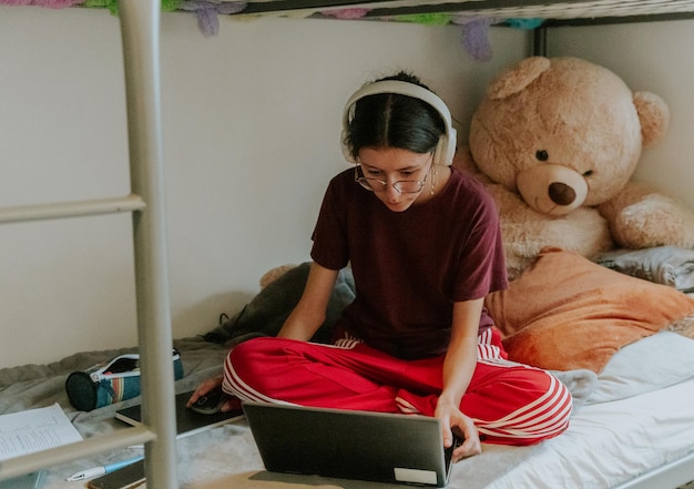 A teenage girl sits on a bed with a computer