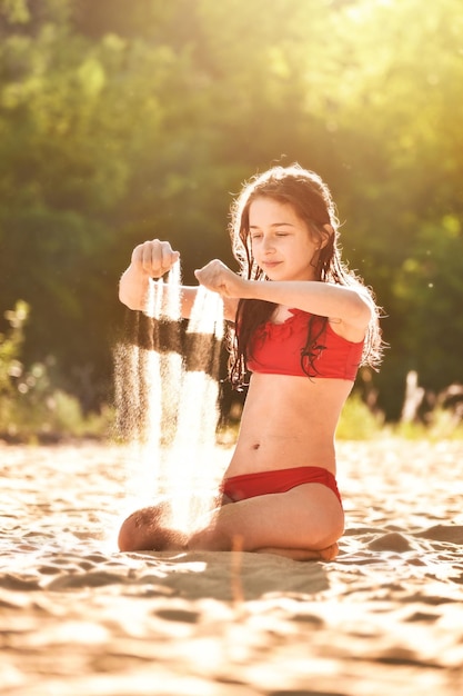 10대 소녀가 강가에 모래 위에 앉아 있다 석양에 빨간 수영복을 입은 소녀