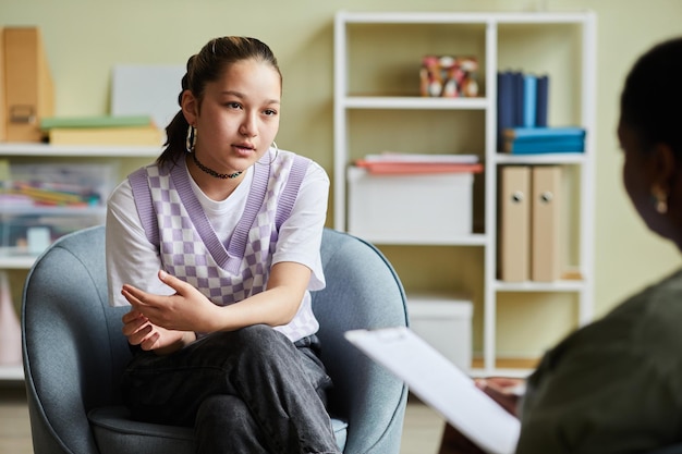 Photo teenage girl sitting on armchair and talking about her problems to psychologist during consultation