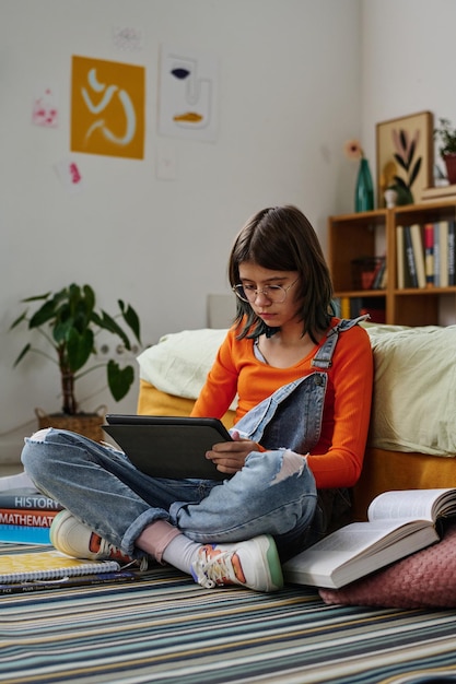 Teenage girl sitting on the floor in her bedroom and using tablet pc to prepare for homework online