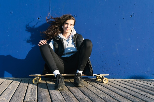 Foto ragazza adolescente seduta su uno skateboard contro il muro