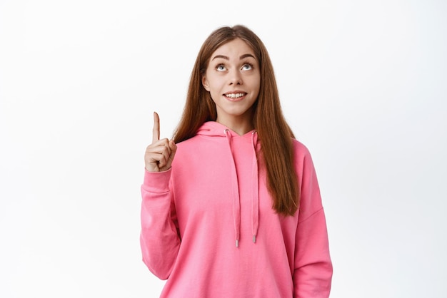 Teenage girl smiles and points up looks at promo deal copyspace on top shows advertisement white background