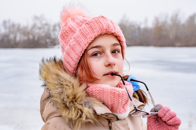 冬に立っている10代の少女。女の子の手に彼女の眼鏡。素晴らしい子供の肖像画