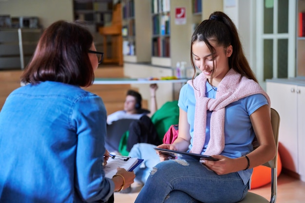 Teenage girl student talking with teacher mentor in the library