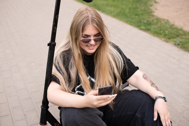 A teenage girl in sunglasses takes a selfie on a scooter